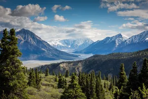 Sweeping vista of snow-capped mountains, lake, and forest.