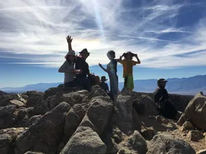 Group of adults and children resting on a mountain hike and waving.